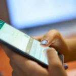 Pessoa digitando no WhatsApp pelo celular, em ambiente de trabalho com notebook ao fundo, representando o uso do aplicativo para ganhar dinheiro online.